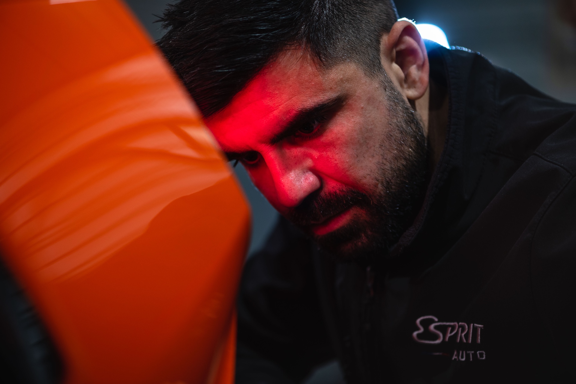 Mécanicien concentré, lumière rouge sur le visage, reflet d'une carrosserie orange